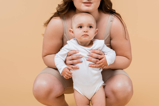 Body positive woman hugging baby daughter isolated on beige  - Фото, зображення