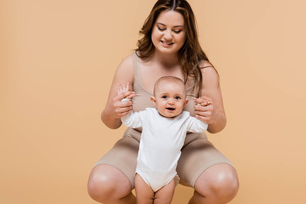 Positive plus size mother holding hands of cheerful daughter isolated on beige  - Foto, immagini