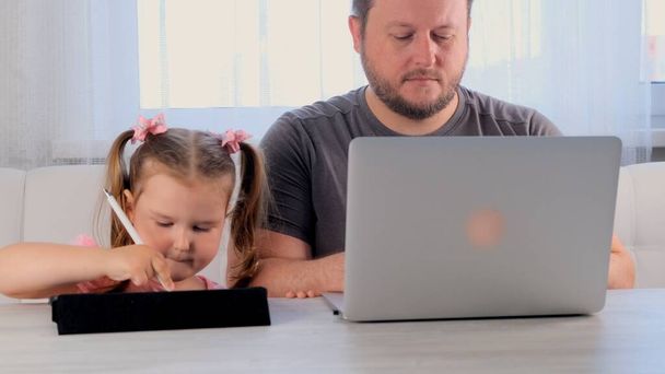 Грустный отец бизнесмена работает над ноутбуком дома рядом с 3-летней девочкой, играющей в планшете. Современная семья. Концепция фрилансера. Зависимость от гаджетов - Фото, изображение
