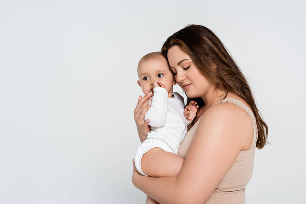 Pretty plus size mother hugging baby daughter isolated on grey - Photo, Image