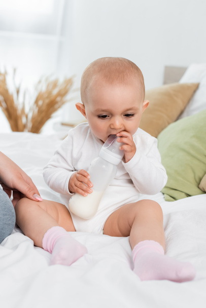 Baby girl holding bottle with milk near mother on bed  - Φωτογραφία, εικόνα