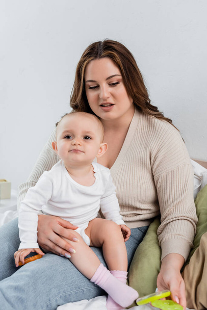 Pretty body positive woman holding child with toy on bed  - Foto, Bild
