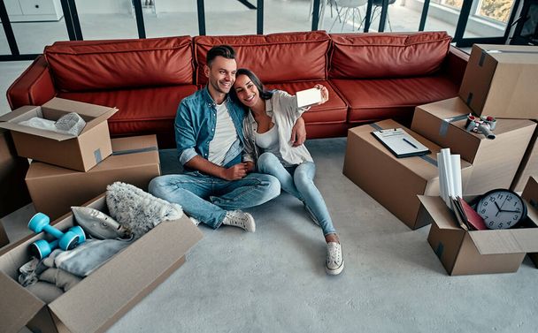 A fiatal pár szelfiket készít az okostelefonjával az új otthonukban. Költözés, házvásárlás, lakás koncepció. - Fotó, kép