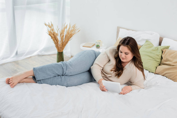 Barefoot plus size woman using digital tablet on bed  - Foto, afbeelding
