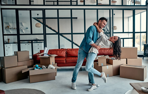 Щаслива безтурботна кавказька пара вперше власники будинків власники оренди танцюють сміючись у вітальні з коробками разом, смішні орендарі отримують задоволення від переїзду в новому будинку в рухомий день
. - Фото, зображення