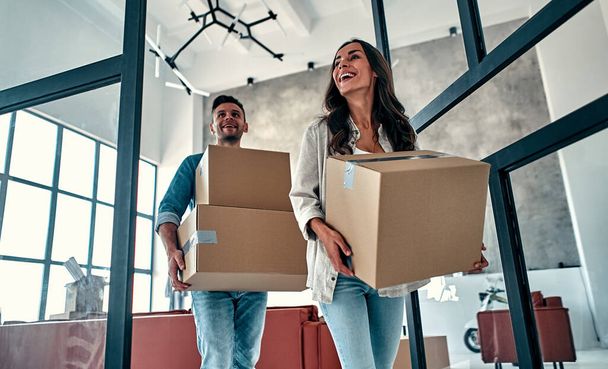 A young married couple in the living room in the house unpack boxes with things. Happy husband and wife are having fun, are looking forward to a new home. Moving, buying a house, apartment concept. - Photo, Image