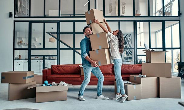 Moving, buying a house, apartment concept. Young couple with a bunch of falling boxes funny trying to catch them. - Foto, Bild