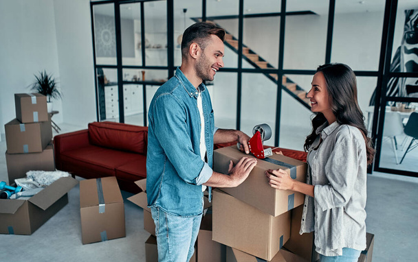 Jovem casal caucasiano embalagem caixa de papelão para se mudar em novo apartamento. - Foto, Imagem