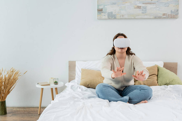 Brünette plus size Frau spielt in Virtual-Reality-Headset auf dem Bett  - Foto, Bild