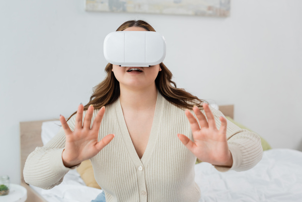 Усміхнена жінка з іграми з надмірною вагою у гарнітурі віртуальної реальності в спальні
  - Фото, зображення
