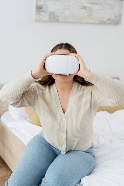 Giovane donna con sovrappeso che gioca in cuffia realtà virtuale in camera da letto  - Foto, immagini