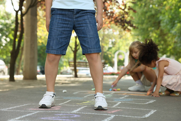 Little children playing hopscotch drawn with chalk on asphalt outdoors, closeup - Фото, зображення