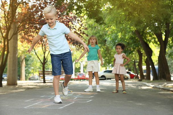 Маленькі діти грають на хмелю, намальованому крейдою на асфальті на відкритому повітрі
 - Фото, зображення