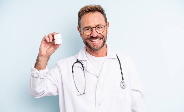 middle age handsome man smiling happily with a hand on hip and confident. physician with pills bottle - Photo, Image