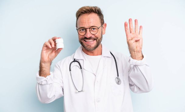 middle age handsome man smiling and looking friendly, showing number four. physician with pills bottle - Photo, Image