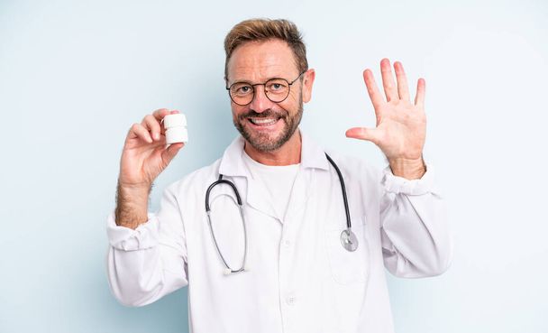 middle age handsome man smiling and looking friendly, showing number five. physician with pills bottle - Photo, Image