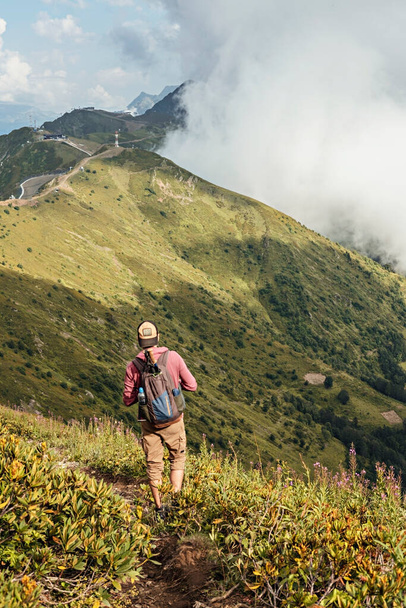 Молодий чоловік з рюкзаком, що ходить по зелених горах Кавказу серед кущів рододендрону, подорожує активним і здоровим життям, пейзажем. - Фото, зображення
