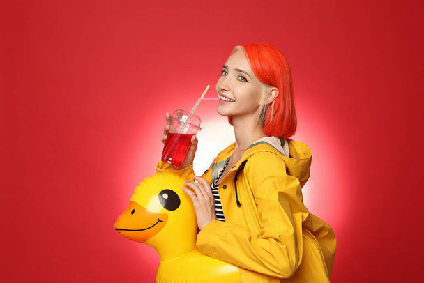 Beautiful young woman with bright dyed hair and inflatable ring drinking refreshing cocktail on color background - Foto, imagen