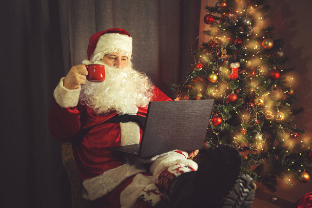Authentic Santa Claus is working on a laptop. Home interior. In anticipation of Christmas and New Years.  - Fotoğraf, Görsel