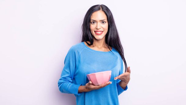 pretty hispanic woman smiling cheerfully, feeling happy and showing a concept. empty bowl concept - Zdjęcie, obraz