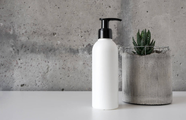 Biała makieta butelki kosmetycznej z pompą i soczysty w betonie garnek na białym biurku na tle ściany cementu - Zdjęcie, obraz