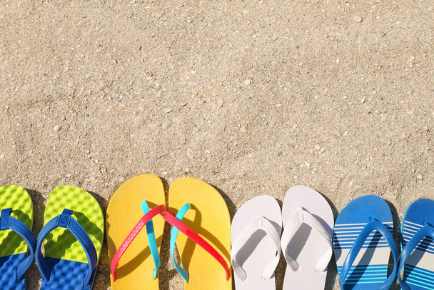 Many different flip flops on sand, flat lay. Space for text - Fotó, kép