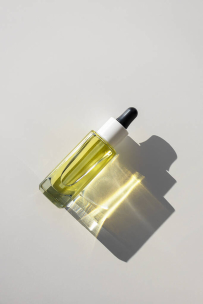 Bouteille de sérum d'huile jaune facial en verre avec pipette sur fond blanc avec réflexion lumineuse du rayon de soleil, vue de dessus - Photo, image