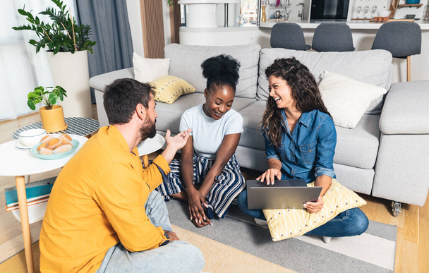 Three young best friends and business partners sitting in apartment gather to celebrate their first online sale on their website of a company they started as a small business for online shopping - Fotografie, Obrázek