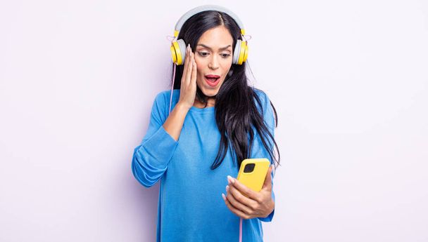 pretty hispanic woman feeling happy, excited and surprised. smartphone and headphones concept - Foto, imagen