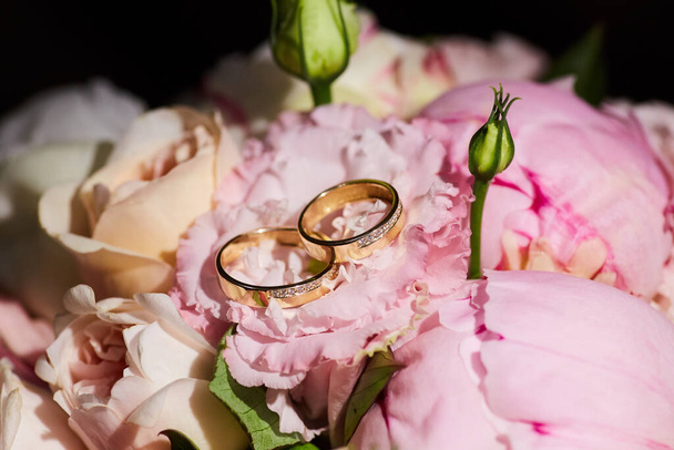 Wedding rings made of metal lie on a beautiful bouquet of fresh flowers. The concept of holidays and ceremonies. - Photo, Image