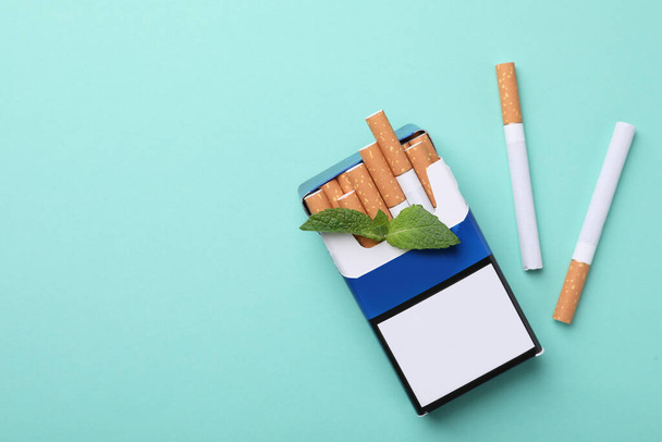 Pack of menthol cigarettes and mint on turquoise background, flat lay. Space for text - Foto, Imagem