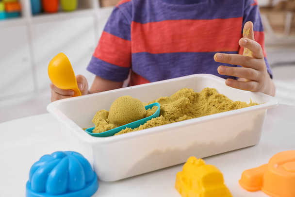Little boy playing with bright kinetic sand at table in room, closeup - Fotografie, Obrázek