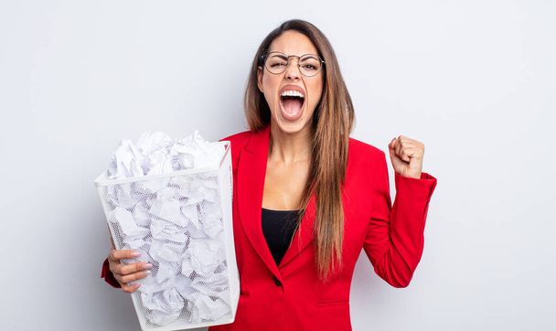 pretty hispanic woman shouting aggressively with an angry expression. paper balls failure concept - Foto, immagini