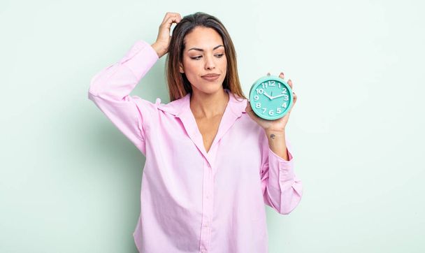 pretty hispanic woman smiling happily and daydreaming or doubting. alarm clock concept - Foto, Imagen