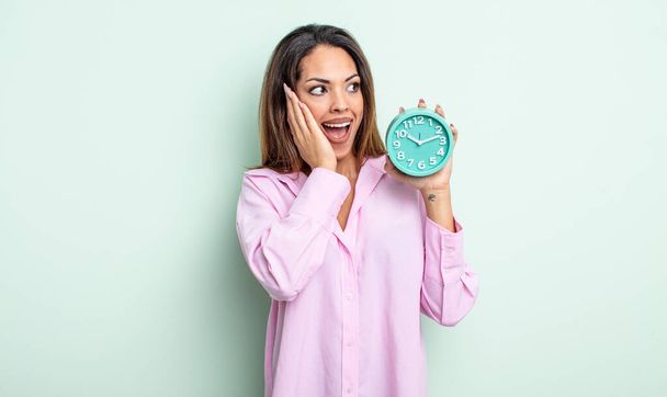 pretty hispanic woman feeling happy, excited and surprised. alarm clock concept - Fotoğraf, Görsel