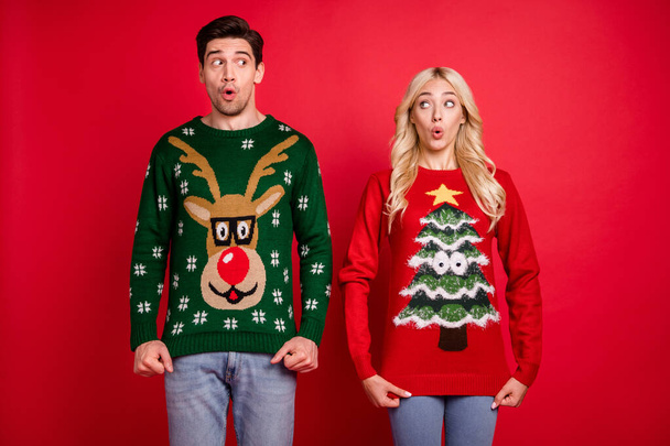 Photo portrait amazed surprised couple wearing ugly sweaters celebrating xmas isolated bright red color background - Foto, immagini