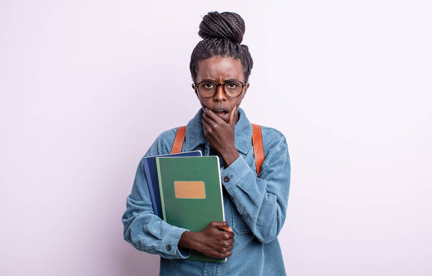 pretty black woman with mouth and eyes wide open and hand on chin. student with books concept - Foto, Imagem