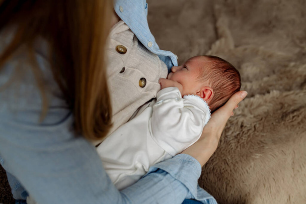 Young mom breastfeeding newborn baby son sitting on bed in bedroom at home - Foto, Bild