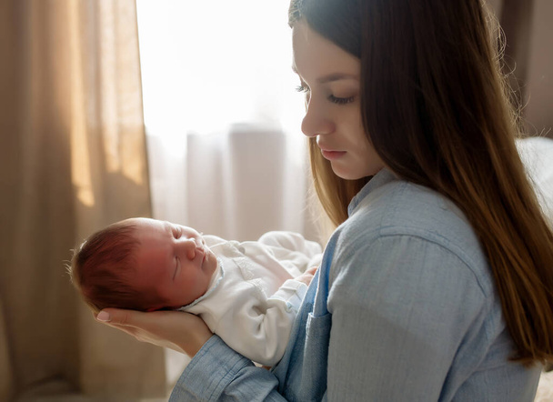 Young beautiful mother with long hair holds a newborn baby son in her arms - Photo, image