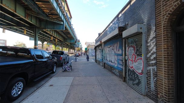 Realiteit van de binnenwijk in het Unionport gebied van de Bronx. Moslim vrouw met hoofddeksel steekt straat over met verhoogde metro trein aan de linkerkant en gesloten vernielde winkels aan de rechterkant. - Foto, afbeelding