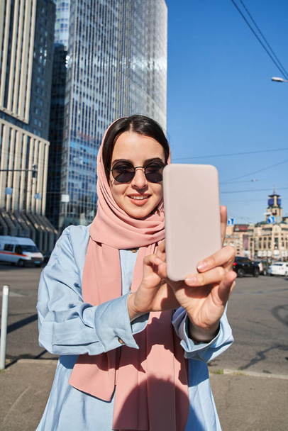 Ευτυχισμένη γυναίκα ισλαμικής θρησκείας ποζάρει στη μεγάλη πόλη κατά τη διάρκεια των ταξιδιών - Φωτογραφία, εικόνα