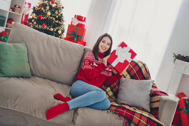 Photo of positive lady sit comfy couch presenting gift box wear pullover in decorated x-mas home indoors - Foto, afbeelding