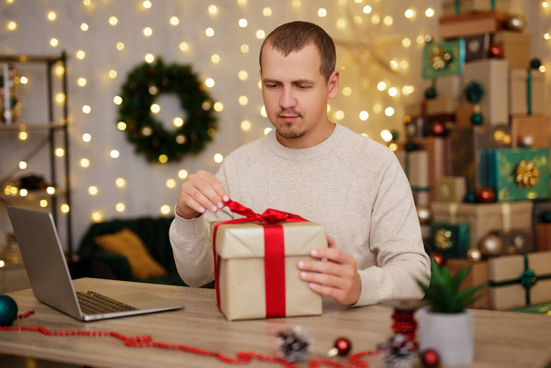 Young man with laptop and gift in christmas interior - Foto, afbeelding