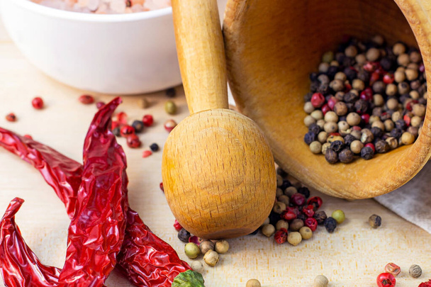 Mix of dried peppercorns in the mortar with pestle, dry chili pepper and salt for cooking on light wooden cutting board background in the kitchen. - Photo, Image