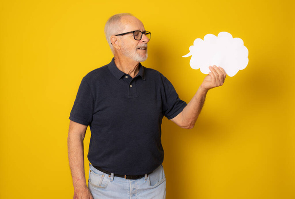 Senior man holding paper cloud isolated over yellow background. - Fotografie, Obrázek