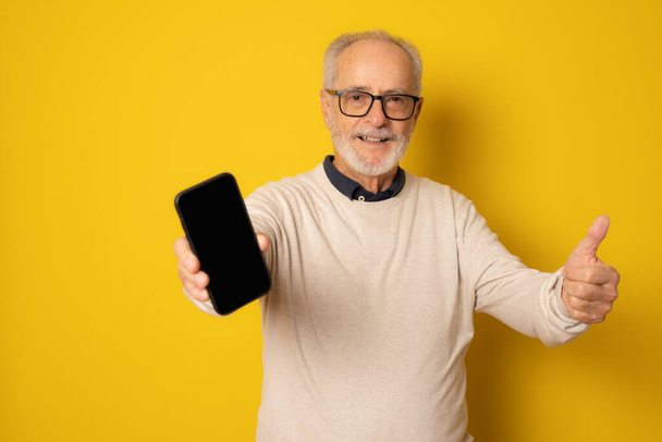 Elämäntapa, tehnologia ja vanhusten käsite: Komea vanha harmaatukkainen mies, joka on pukeutunut älykkääseen rentoon tyyliin älypuhelimella ja hymyilee keltaisella taustalla - Valokuva, kuva
