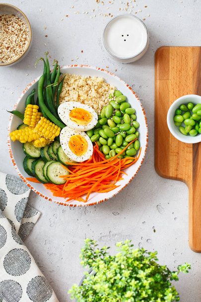 Healthy salad with couscous, carrots, cucumber, green beans, soybeans, corn and an egg on a gray concrete background. Food and health. Buddha bowl salad. Organic natural foods. Plant-based dishes. - Photo, Image