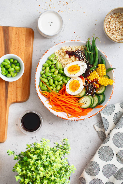 Egészséges saláta kuszkusz, sárgarépa, uborka, zöldbab, szójabab, kukorica és egy tojás szürke beton háttérrel. Étel és egészség. Buddha tál saláta. Szerves természetes ételek. Növényi alapú ételek. - Fotó, kép