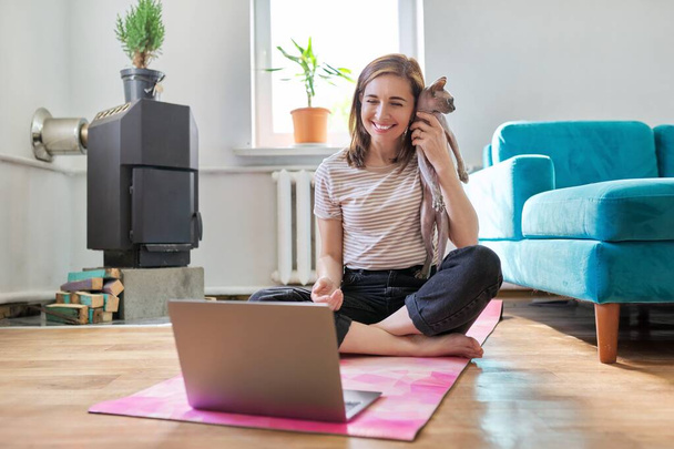 Middle-aged smiling woman with laptop and cat on the floor - Fotoğraf, Görsel