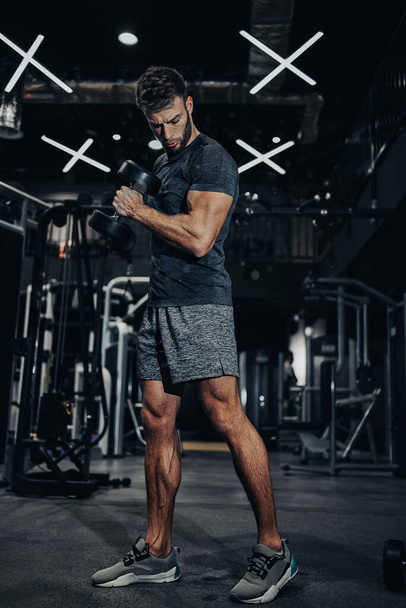 Good looking handsome male athlete exercising in modern fitness gym. Dark muddy light with strong shadows. Indoors sport concept. - Photo, Image